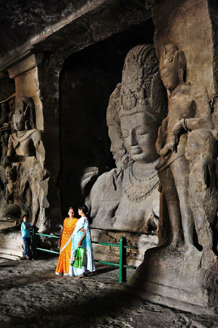 Ancient civilizations artifacts with large stone sculptures in a cave, accompanied by visitors in colorful attire.
