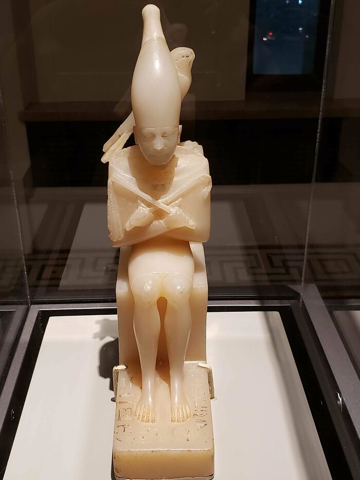 Ancient artifact in a museum display, depicting a seated figure with a tall headdress, offering insights into past civilizations.