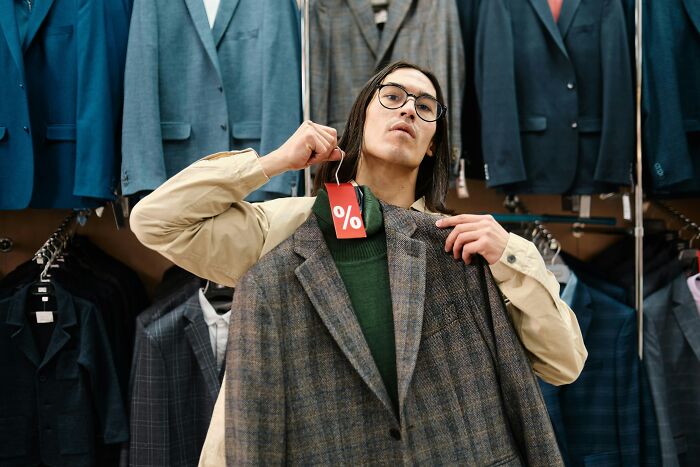 Man holding a plaid blazer with a sale tag in a suit store, showcasing recent fashion trends people hate.