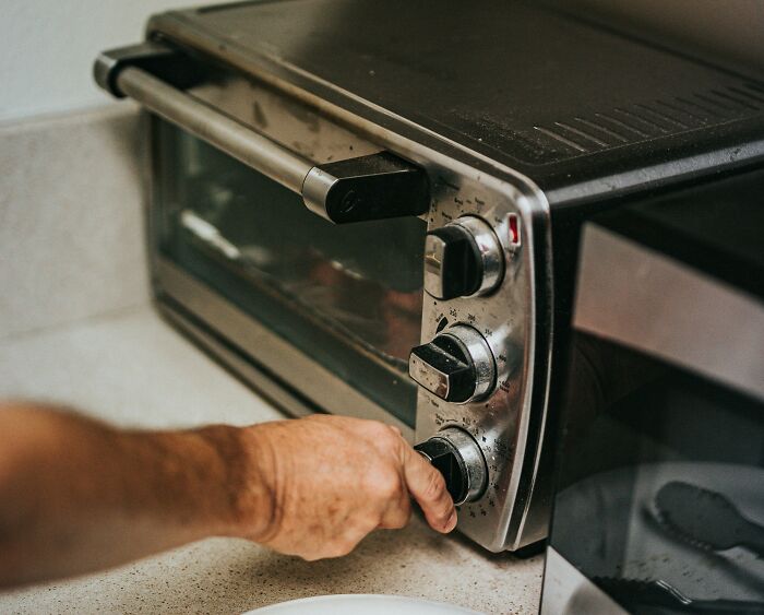 A hand adjusting a k**b on a multifunctional oven toaster, highlighting versatility.