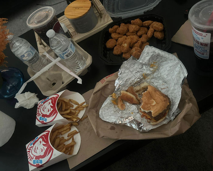 Fast food on a table, possibly left by annoying boyfriends or husbands, including fries, burgers, nuggets, and drinks.