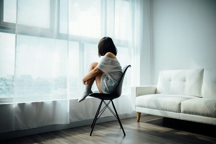 Person sitting on a chair by a window, reflecting on mindset change, with a sofa nearby in a softly lit room.