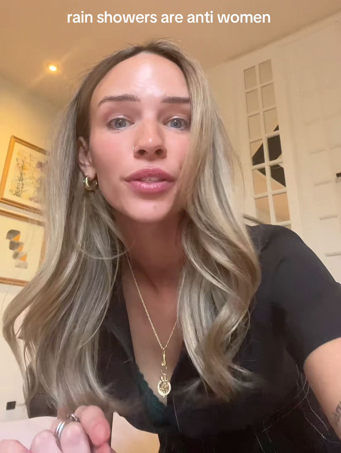 Woman expressing opinion on rain showers being anti-women, indoors, with text overlay above her head.