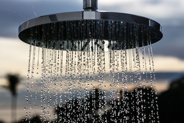 Close-up of rain showers falling from a metal showerhead against a blurred sky.