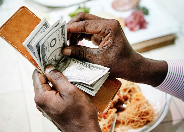 A person counting money from a wallet over a plate of pasta, sparking a debate on tipping etiquette.