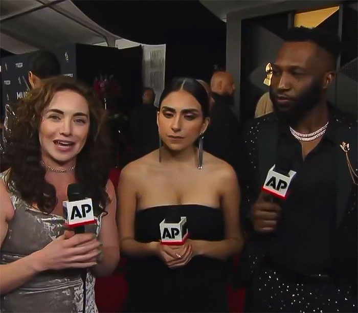 Three reporters with microphones during the Grammys event, discussing Chappell Roan and R&B legend snubbing controversy. Three reporters with microphones during the Grammys event, discussing Chappell Roan and R&B legend snubbing controversy.