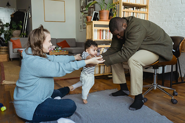 Couple playing with baby in a cozy living room, surrounded by books and plants.
