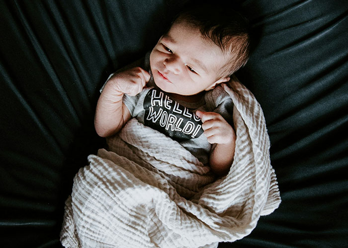 Baby wrapped in a blanket with a "Hello World!" shirt, illustrating baby name preferences.