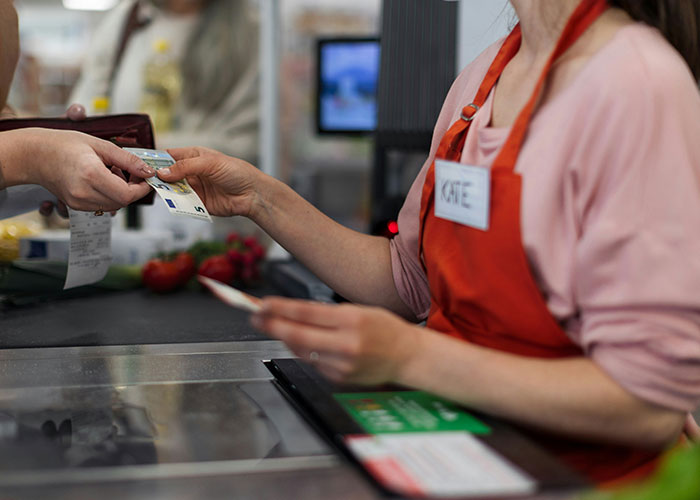 Person at a checkout counter handing a card to a cashier named Kate, highlighting customer interaction.