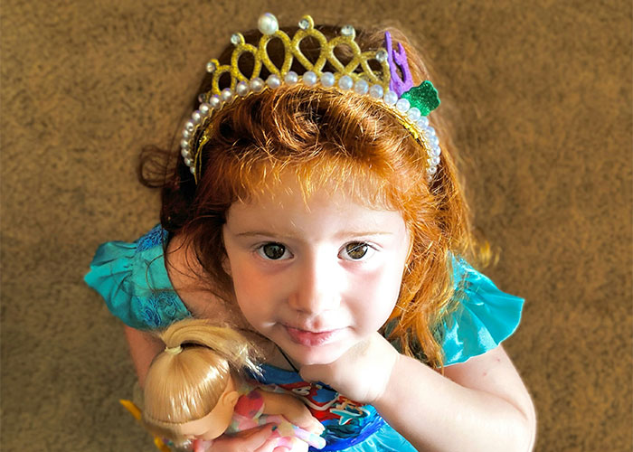 Red-haired child in a crown holding a doll, illustrating baby names topic.