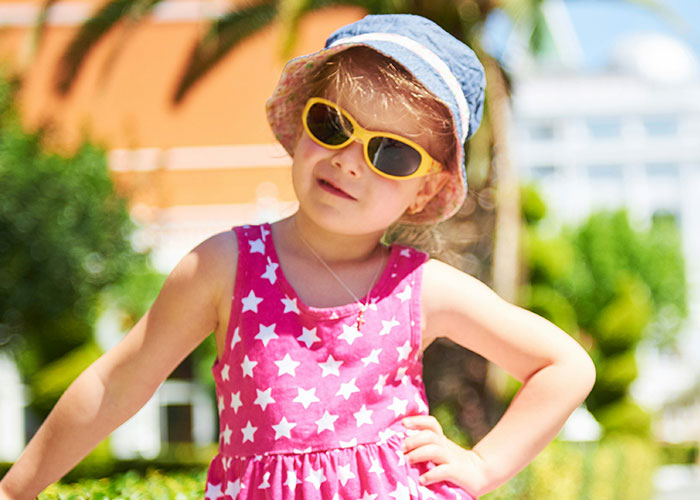 Child in sunglasses and a starry pink dress outdoors, highlighting trendy baby names.