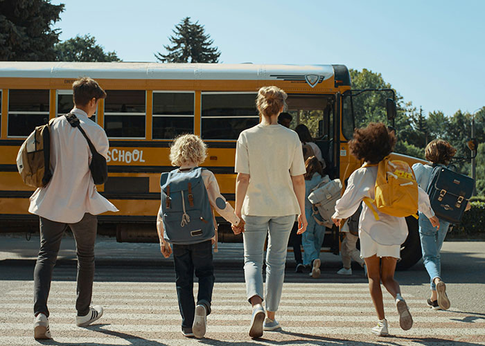 Children walking towards a school bus with backpacks on a sunny day.