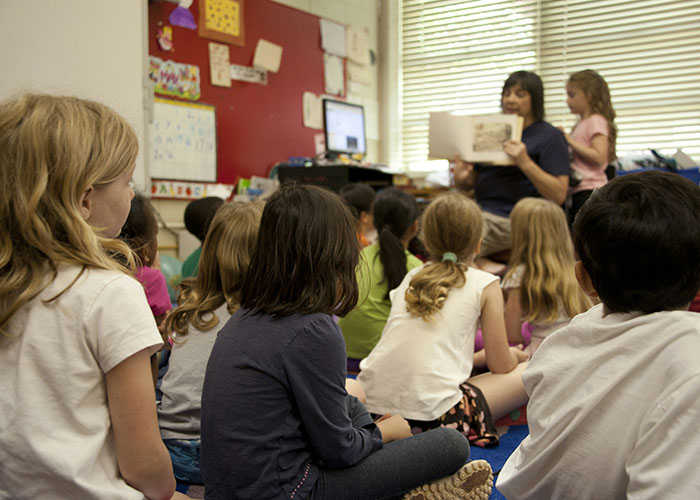 Children listen to a teacher reading a book in a classroom, highlighting reactions to unconventional baby names.