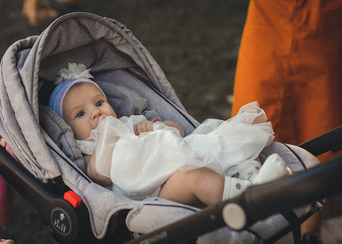 Baby in a stroller wearing a white dress and headband, illustrating the concept of baby names and parental perception.