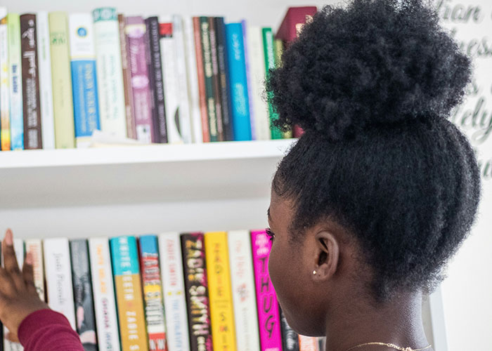 Person browsing a bookshelf filled with various books, focusing on a selection of baby name guides.