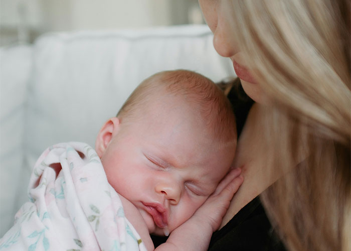 Mother cradling a sleeping baby, wrapped in a blanket, illustrating a discussion on baby names causing loss of respect.
