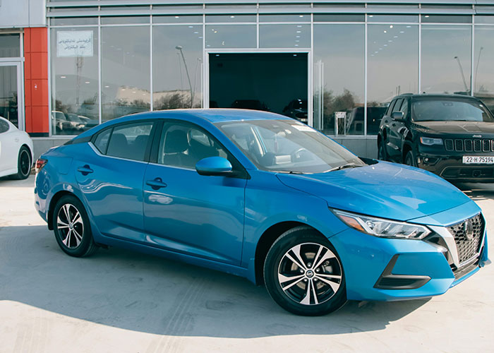 A blue sedan car parked in front of a dealership building under a clear sky.