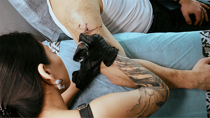 Tattoo artist inking a design on a man's arm, showcasing wild artwork.