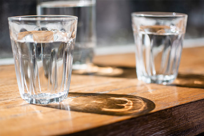 Glasses of water casting shadows on a wooden bar surface, representing memorable moments for bartenders.