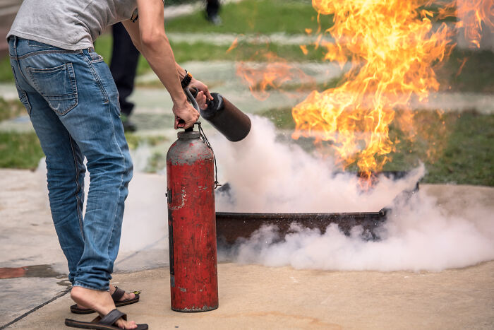 Person using fire extinguisher on outdoor fire, showcasing unique gift ideas for someone who has everything.