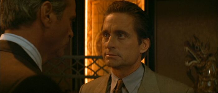 Two men in suits having a conversation indoors, reminiscent of celebrities in the 90s.