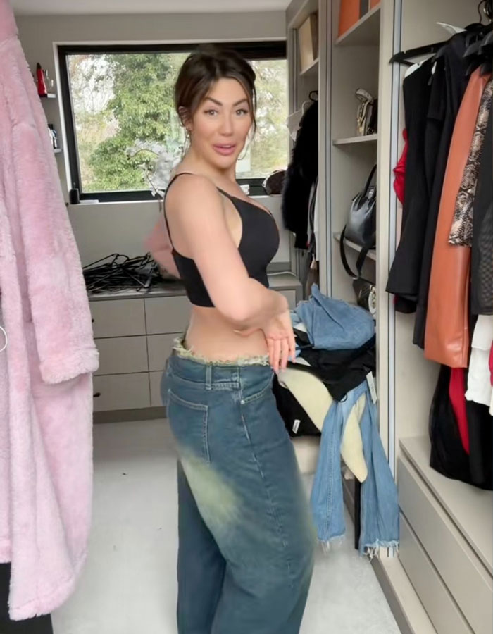 Woman showing new figure in a closet, wearing a black top and jeans, highlighting transformation after BBL removal.