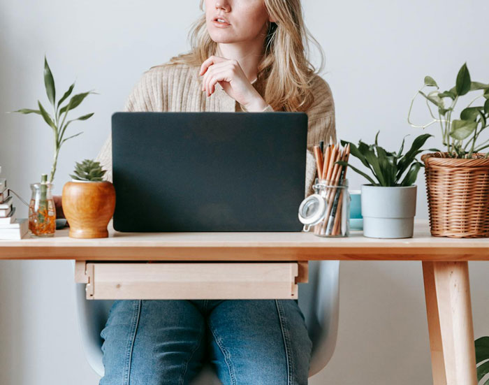 Woman at a desk with laptop, surrounded by plants, considering a plan involving a lie. Woman at a desk with laptop, surrounded by plants, considering a plan involving a lie.