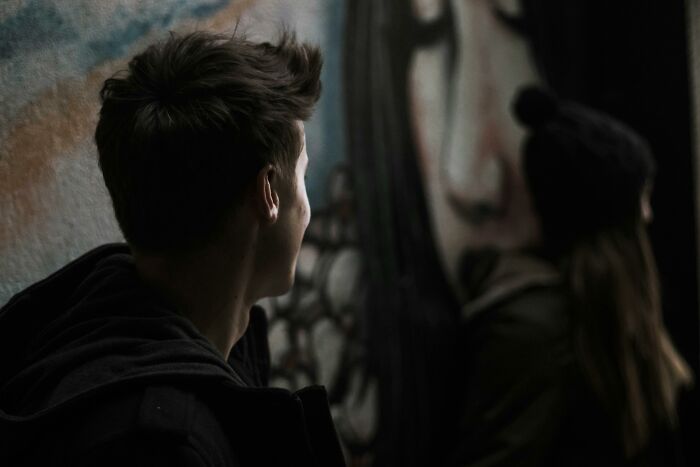 Person looking at a woman standing by a mural, suggesting intrigue and tension. Person looking at a woman standing by a mural, suggesting intrigue and tension.