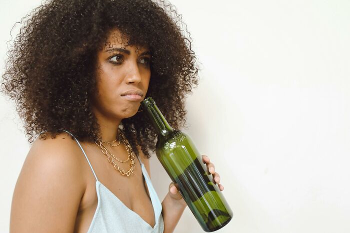 Woman looking uncomfortable while holding a bottle, worried about boyfriend's friend being her online stalker. Woman looking uncomfortable while holding a bottle, worried about boyfriend's friend being her online stalker.