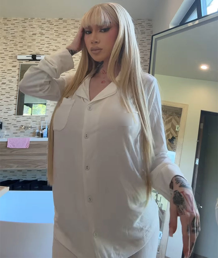 Woman in a white outfit with long blonde hair and tattoos, in a modern bathroom setting. Woman in a white outfit with long blonde hair and tattoos, in a modern bathroom setting.