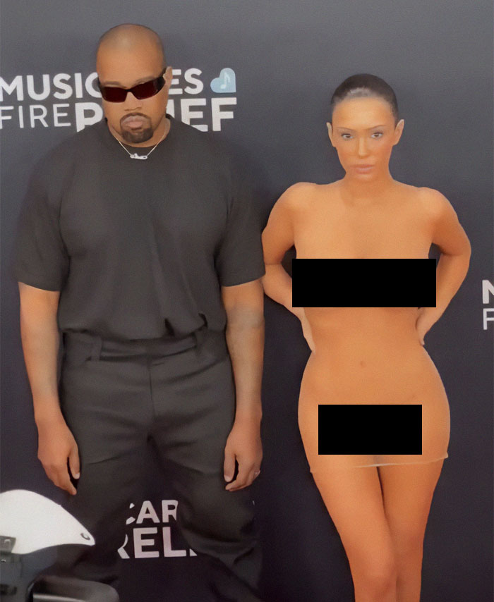 Man in black attire with a woman in an eye-catching outfit on a red carpet event backdrop. Man in black attire with a woman in an eye-catching outfit on a red carpet event backdrop.