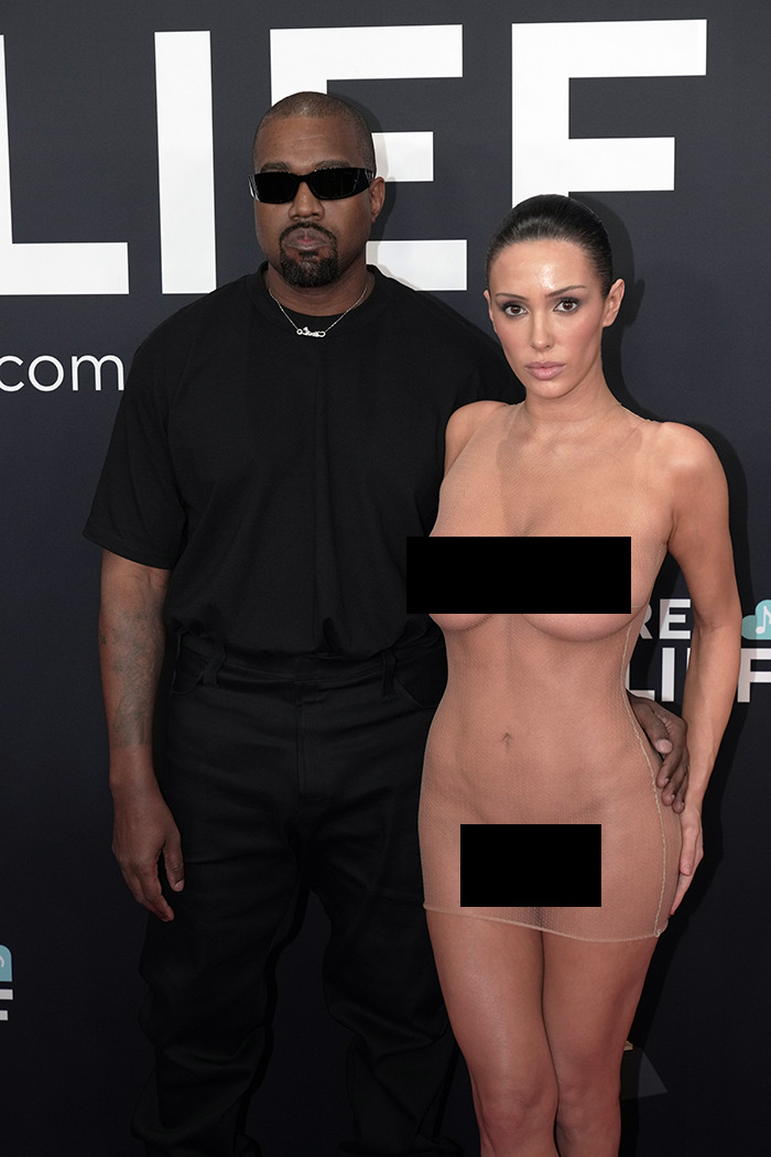 Bianca Censori and Kanye West posing at the Grammys red carpet, dressed in a black outfit and a sheer dress.