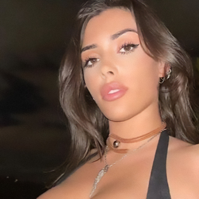 Bianca Censori with long hair and a necklace, posing outdoors at night.