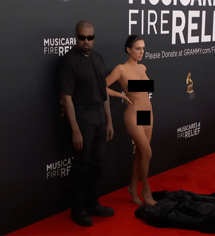 Man and woman on Grammys red carpet; woman in bold outfit, attracting attention. Man and woman on Grammys red carpet; woman in bold outfit, attracting attention.