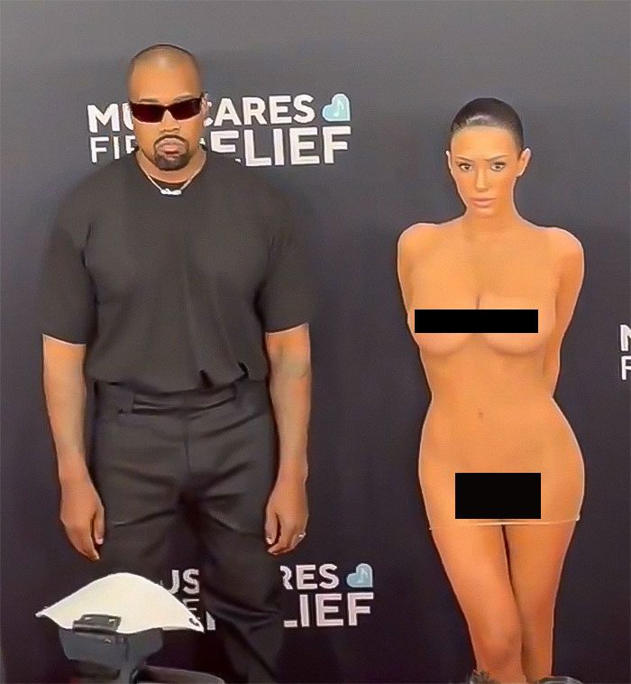 Man in black outfit and sunglasses standing next to woman in minimal attire at event, related to Kanye West and Bianca Censori.