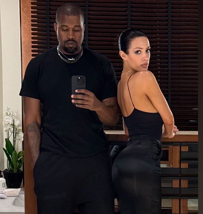 People standing together indoors, one taking a mirror selfie, related to Bianca Censori and response to Twitter tirade.