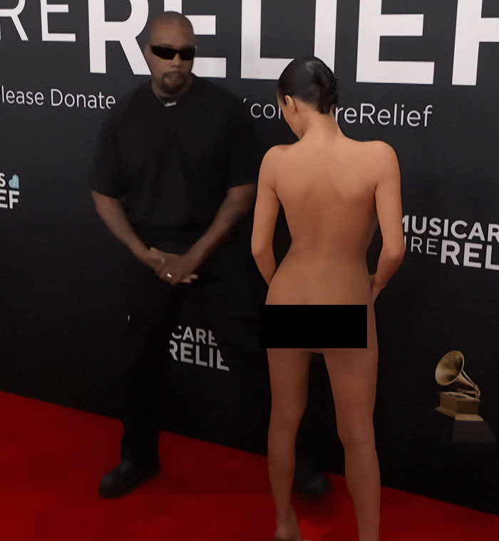 Bianca Censori in controversial dress at Grammys event, standing on red carpet next to a man in black. Bianca Censori in controversial dress at Grammys event, standing on red carpet next to a man in black.