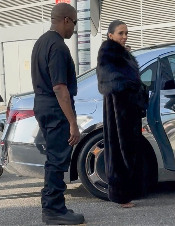 Bianca Censori in a fur coat near a car, with Kanye West in casual attire standing beside her. Bianca Censori in a fur coat near a car, with Kanye West in casual attire standing beside her.