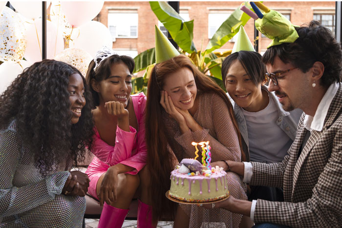 Friends celebrating a lady's birthday with cake, wearing party hats and smiling.