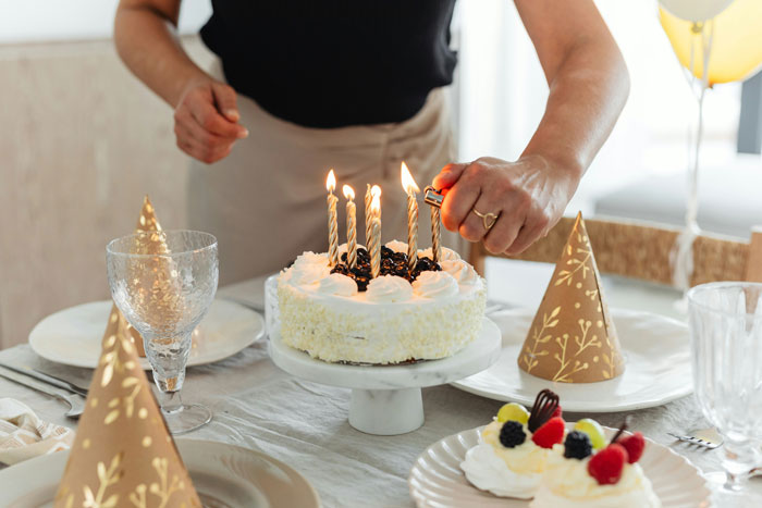 Lighting candles on a birthday cake with party hats on the table for a lady's celebration.