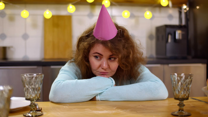 Woman in birthday hat looking pensive at a party, reflecting high celebration costs discussed online.