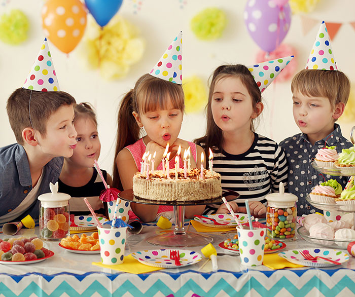 Children at a birthday party, wearing colorful hats, blowing out candles on a cake, around a festive table. Children at a birthday party, wearing colorful hats, blowing out candles on a cake, around a festive table.