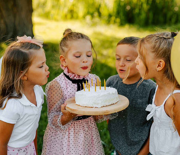 Children at a birthday party blowing out candles on a cake outdoors. Children at a birthday party blowing out candles on a cake outdoors.