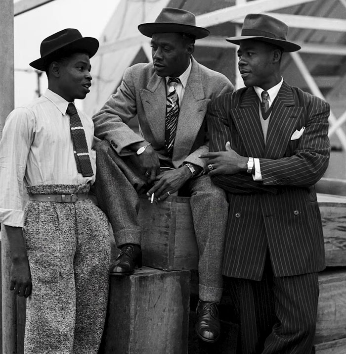 Three men in stylish suits and hats, engaging in conversation, symbolize classic fashion. Three men in stylish suits and hats, engaging in conversation, symbolize classic fashion.