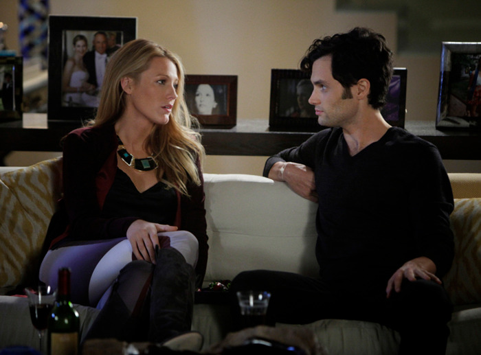 Blake Lively in conversation on a couch with Penn Badgley, surrounded by picture frames in a scene from "Gossip Girl.
