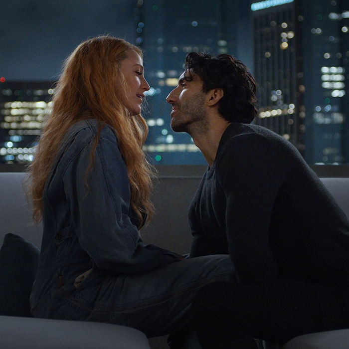 A couple sitting closely on a rooftop at night, with a city skyline in the background, capturing an intimate moment.
