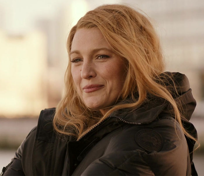 A woman in a black coat outdoors, with long blonde hair, associated with Ryan Reynolds' past relationships.