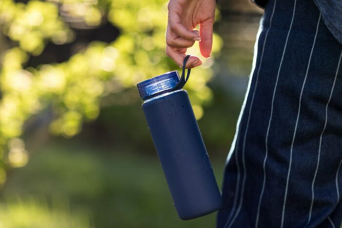 Person carrying a blue travel water bottle outdoors, a must-have for packing efficiently.