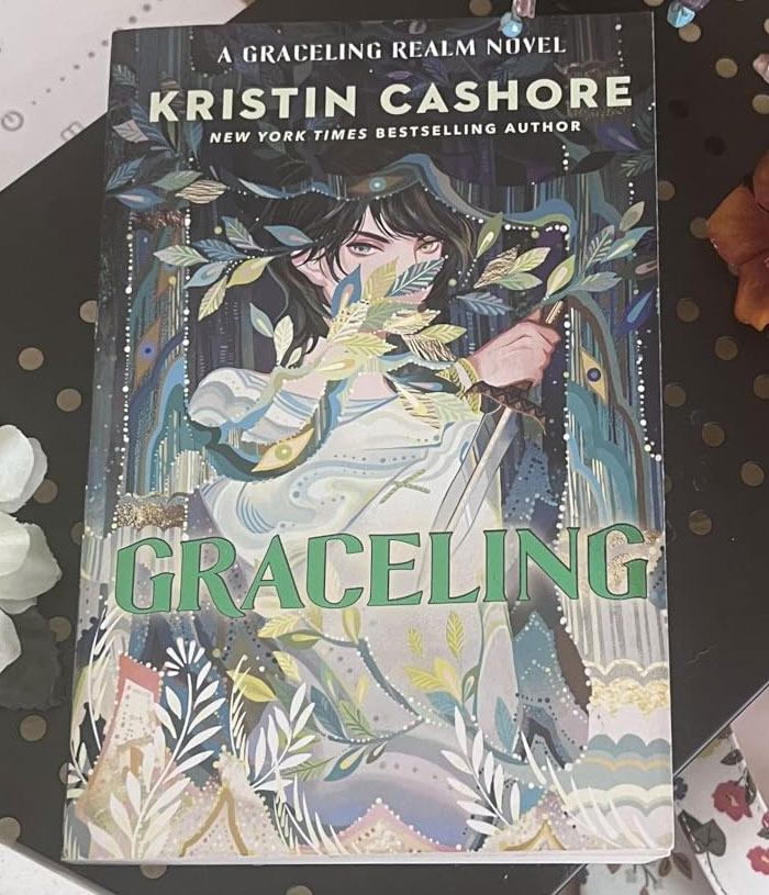 "Graceling book cover by Kristin Cashore, featuring an illustrated character amidst foliage and patterns."