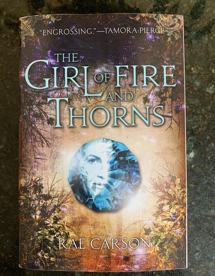 Cover of "The Girl of Fire and Thorns" by Rae Carson, featuring a mystical gemstone and a woman's face.
